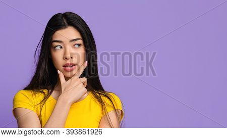 Curious Young Korean Lady Looking At Copy Space On Purple Background With Interest, Thinking About G