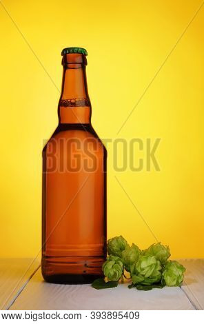 Glass Bottle Of Fresh Beer With Green Hop Cones On Light Wooden Table Over Yellow Background.
