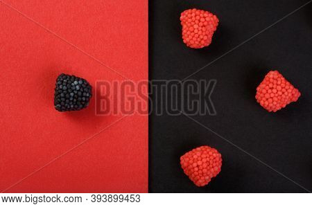 Red Chewing Candies In Form Of Raspberry On Red Background And One Black Candy Flavored Blackberry O
