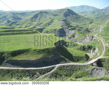 A Series Of Majestic Green Mountains Stretches To The Horizon, Through Which Winding Roads Wind.
