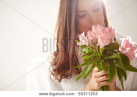 Portrait of lovely lady looking at bunch of flowers in her hands
