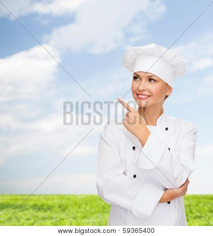 cooking, advertisement and food concept - smiling female chef, cook or baker pointing finger to something