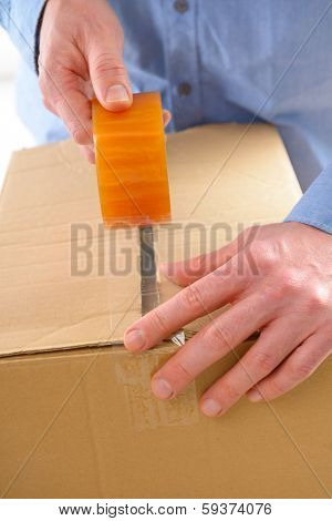 Hands with roll of transparent packaging, adhesive tape on a cardbox