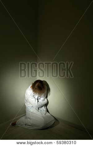 Mentally ill man in strait-jacket in room corner