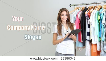 Beautiful young stylist near rack with hangers