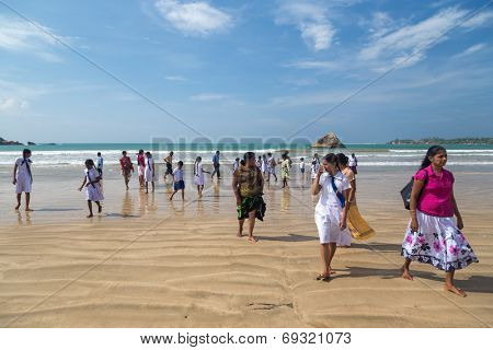 WELIGAMA, SRI LANKA - MARCH 7, 2014: Group of local people walking on sandy beach. Weligama is one of most popular Sri Lankan beaches,