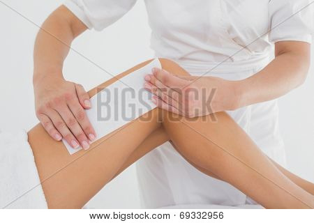 Mid section of therapist waxing woman's leg at spa center