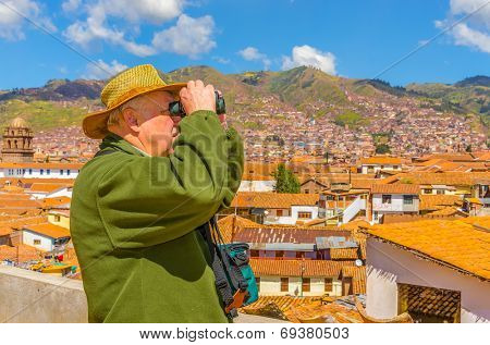 Senior tourist with binoculars watches citiscape in Cusco, Peru