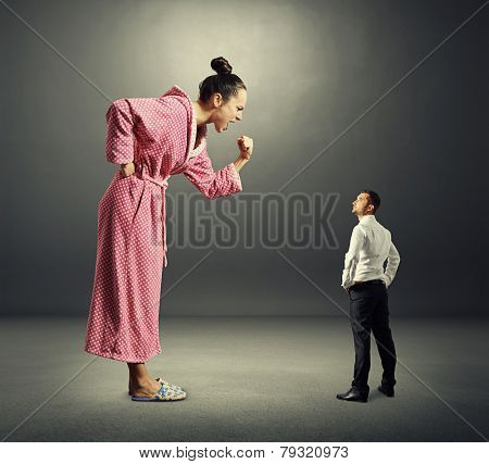 small serious man in black suit looking at big angry woman in pink dressing gown. photo over dark background