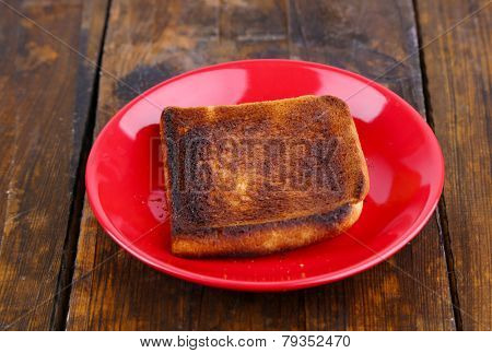Burnt toast bread on red plate, on wooden table background