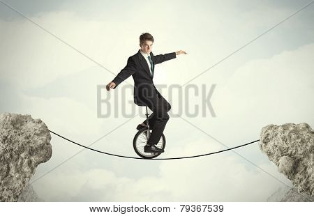 Brave business man riding an mono cycle between cliffs concept