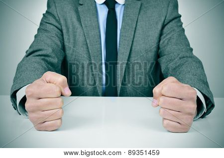 closeup of a young caucasian man wearing a gray suit banging his fists on his office desk