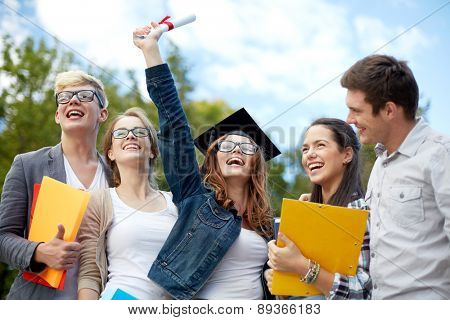 education, graduation and people concept - group of smiling students in mortarboard with diploma and school folders