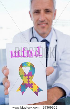 The word mind and portrait of a male doctor showing a blank prescription sheet against autism awareness ribbon