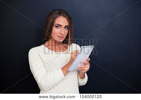 Portrait of a beautiful young woman making notes in notepad over gray backgroundd