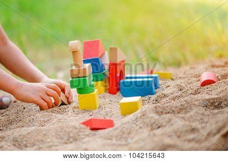 child building toy houses of colorful wooden bricks in sandbox