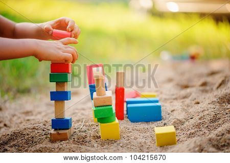 child building toy houses of colorful wooden bricks in sandbox