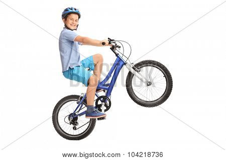 Joyful little boy performing a wheelie with his bike and looking at the camera isolated on white background