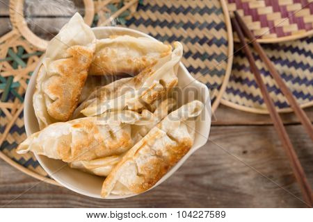 Top view fresh pan fried dumplings on bowl with hot steams. Asian gourmet on rustic vintage wooden background.