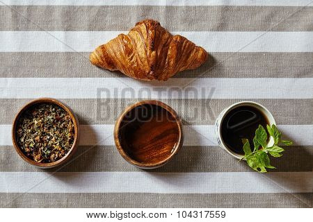 Croissant With Herbs And Honey And Cup Filled With Black Tea And Mint Top View