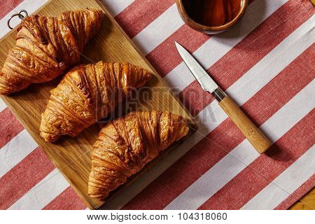 Three French Freshly Baked Croissants On Wooden Plate With Honey Pot And Knife On Striped Cloth