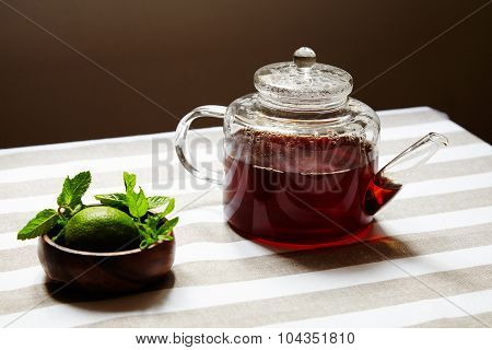 Tea In Transparent Teapot And Wooden Box With Lime And Mint Leaves On Striped Cloth