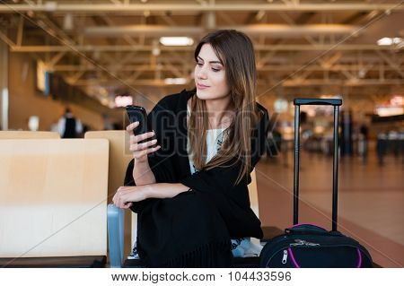 Young female passenger on smart phone at gate waiting in terminal