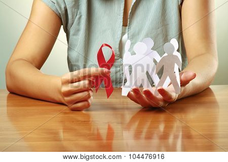 A woman holding paper peolple and an aids red ribbon