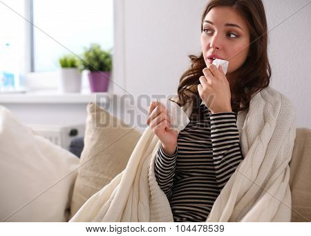 Portrait of a sick woman blowing her nose while sitting on the sofa