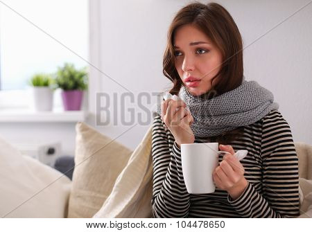 Portrait of a sick woman blowing her nose while sitting on the sofa