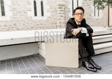 Businessman in a city street sitting next to blank banner