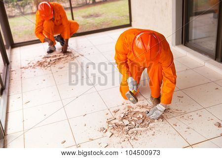 contractors removing old floor tiles using hammer and chisel 