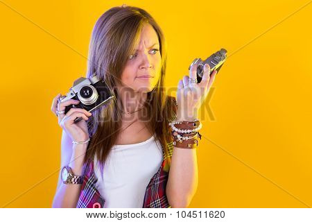 Portrait Of Funny Girl With Two Cameras In Their Hands. Stares At The Camera. Isolation On A Yellow