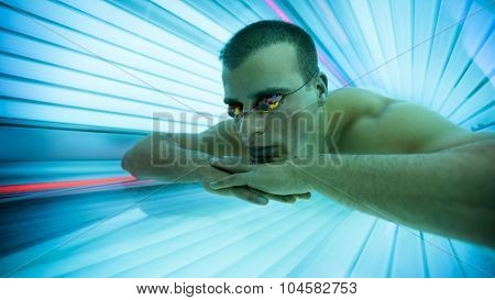 Man with protect glasses on tanning bed in solarium