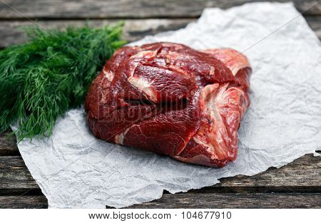 Raw Ox Cheek On Crumpled Paper,  Decorated With Dill. On Old  Wooden Table