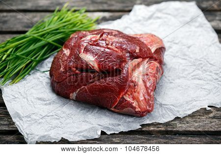 Raw Ox Cheek On Crumpled Paper,  Decorated With Vegetables. On Old  Wooden Table