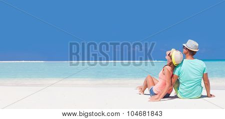 back view of romantic couple in bright clothes enjoying sunny day at tropical beach