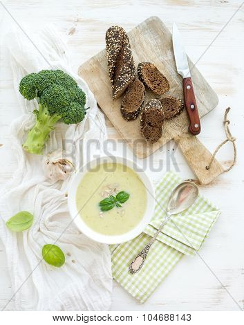 Broccoli cream soup with sunflower seeds, fresh basil and bread in bowl over white wooden table