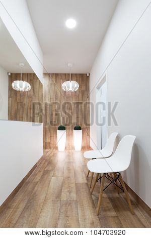 Modern waiting room, reception. Cozy minimalistic interior with seats, lights, mirror and parquet floor.