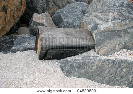 The Body Of An Old Tv Set Among Large Stones Half-strewn Sand With Remains Of Shells. Analog Vacuum