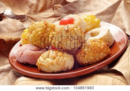 an earthenware plate with some different panellets, typical pastries of Catalonia, Spain, eaten in All Saints Day, on a surface full of dry leaves