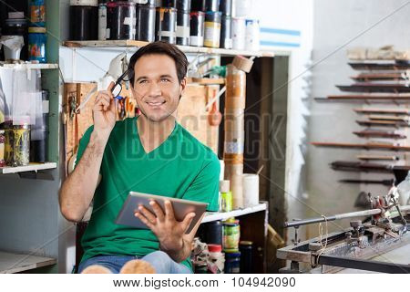 Thoughtful worker holding eyeglasses and tablet computer in paper factory