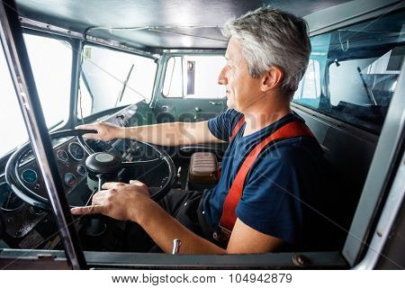 Side view of mature fireman driving firetruck at station