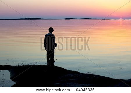 silhouette of a man looking at a Norwegian landscape in the midnight sun
