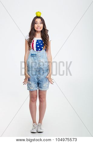 Full length portrait of a beautiful woman standing with apple on the head isolated on a white background