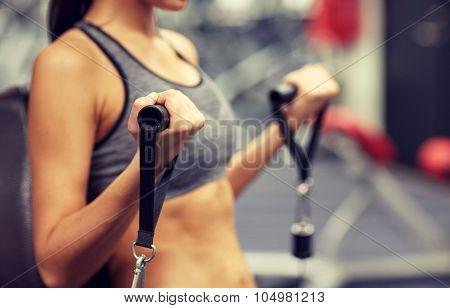 sport, fitness, lifestyle and people concept - close up of young woman flexing muscles on cable gym machine