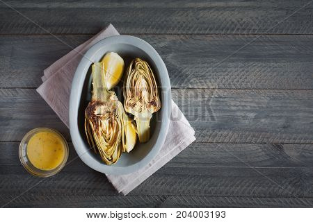 Artichokes and lemons on the plate. This product has one of the highest antioxidant capacities. Traditional vegetables in italian cuisine. Gray wooden background