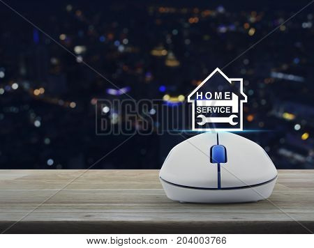 Hammer and wrench and house icon with wireless computer mouse on wooden table over blur colorful night light city tower Home service concept