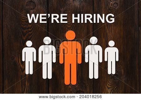 Business concept. Paper men on wooden background and text WE'RE HIRING. Abstract conceptual image