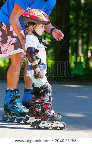 Portait of cute baby boy with inline skating instructor in the park learining to skate.